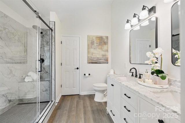 bathroom featuring a marble finish shower, toilet, vanity, wood finished floors, and baseboards