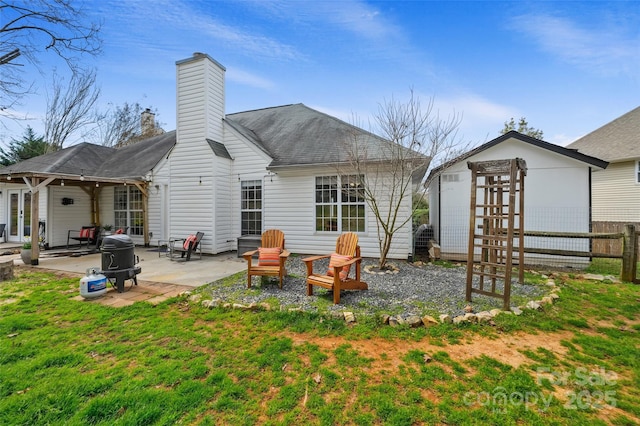 back of property with a patio, a fire pit, fence, a lawn, and a chimney