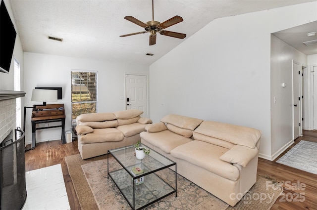 living area featuring lofted ceiling, a brick fireplace, ceiling fan, and wood finished floors