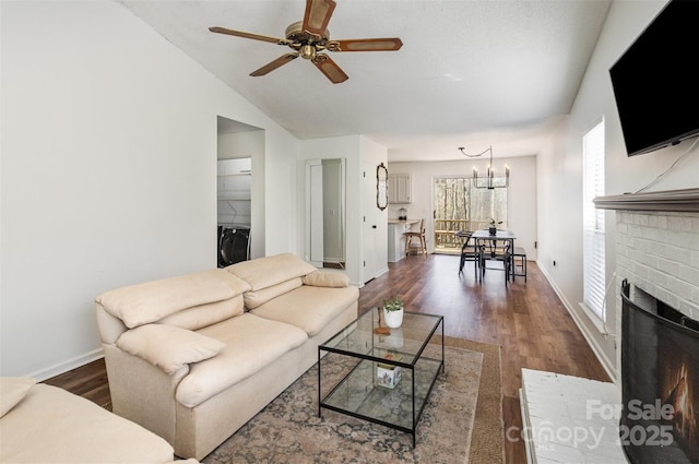 living area featuring a fireplace, vaulted ceiling, wood finished floors, baseboards, and ceiling fan with notable chandelier