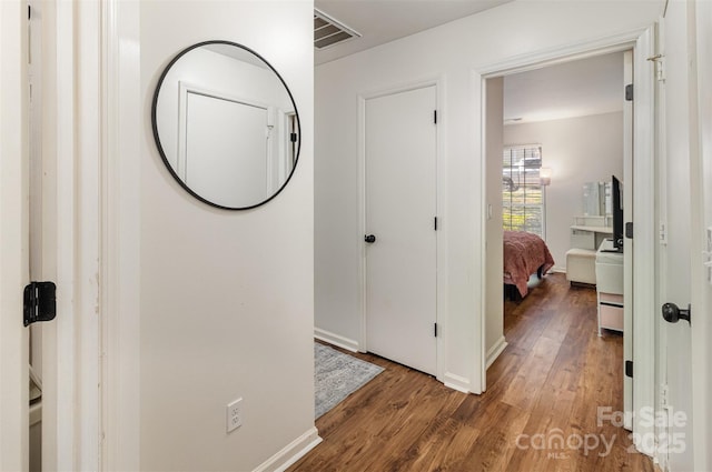 hallway featuring visible vents, baseboards, and wood finished floors