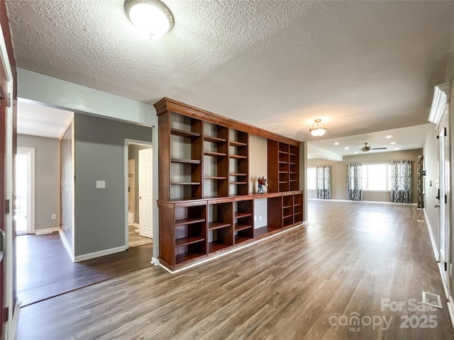 unfurnished living room featuring visible vents, a textured ceiling, baseboards, and wood finished floors