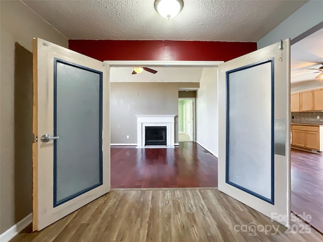 interior space with a fireplace with flush hearth, a textured ceiling, ceiling fan, and wood finished floors