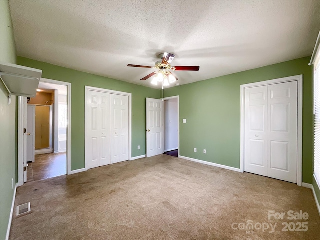 unfurnished bedroom with a textured ceiling, two closets, carpet flooring, and visible vents