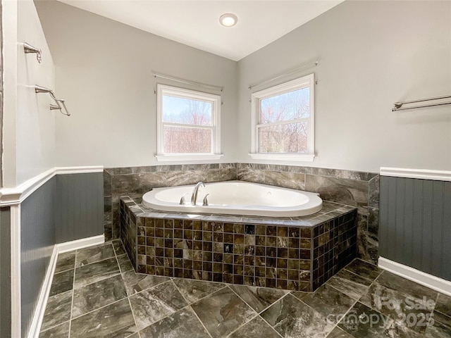 bathroom with a relaxing tiled tub and a wainscoted wall