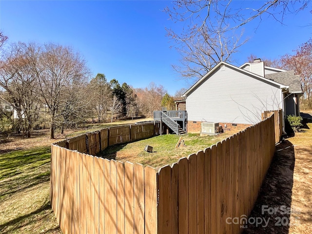 view of side of home featuring a fenced backyard, a chimney, stairway, cooling unit, and a yard