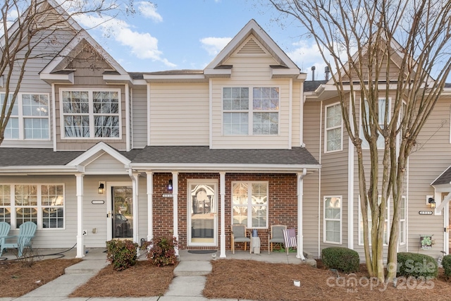 townhome / multi-family property featuring covered porch, brick siding, and roof with shingles