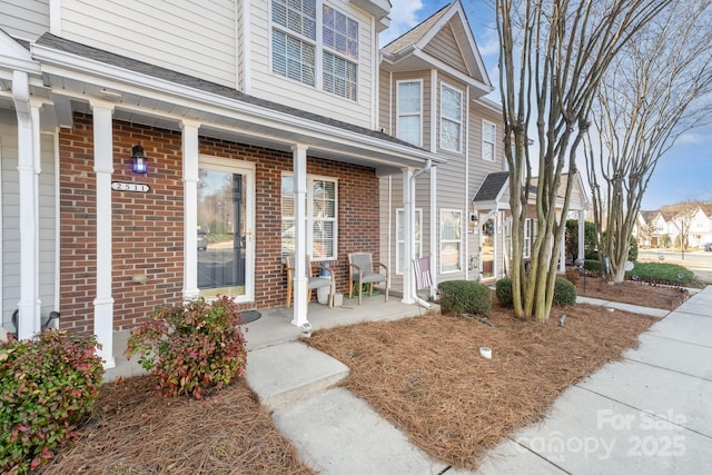 view of exterior entry with a porch and brick siding