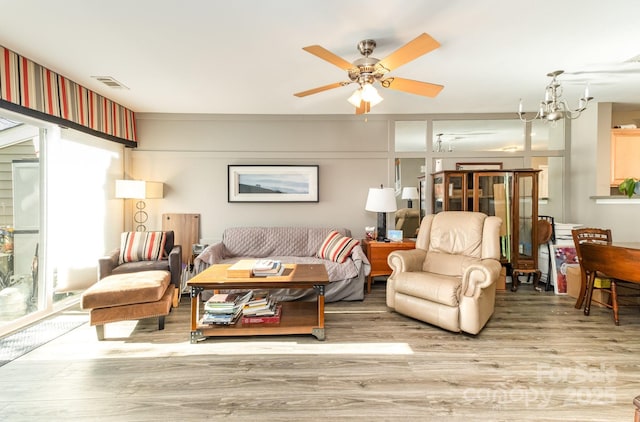 living room featuring visible vents, wood finished floors, and ceiling fan with notable chandelier