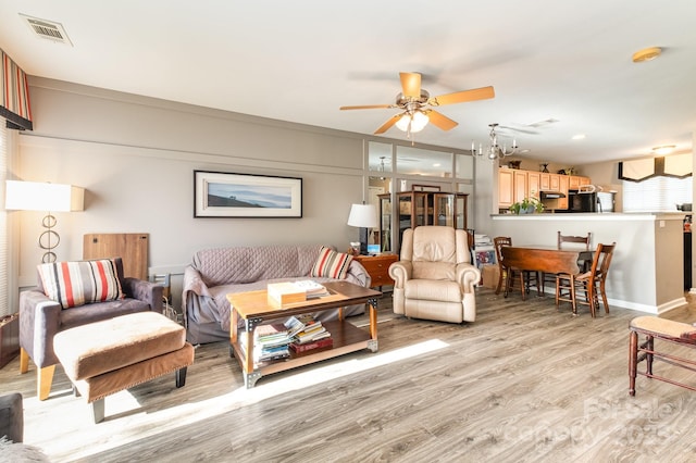 living room featuring light wood-type flooring, visible vents, and ceiling fan with notable chandelier