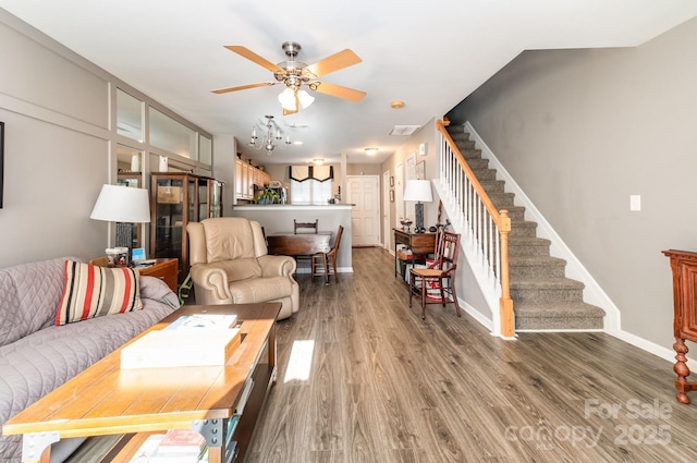 living area with baseboards, ceiling fan, stairway, and light wood finished floors