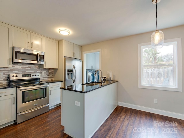 kitchen featuring dark countertops, backsplash, appliances with stainless steel finishes, a sink, and separate washer and dryer