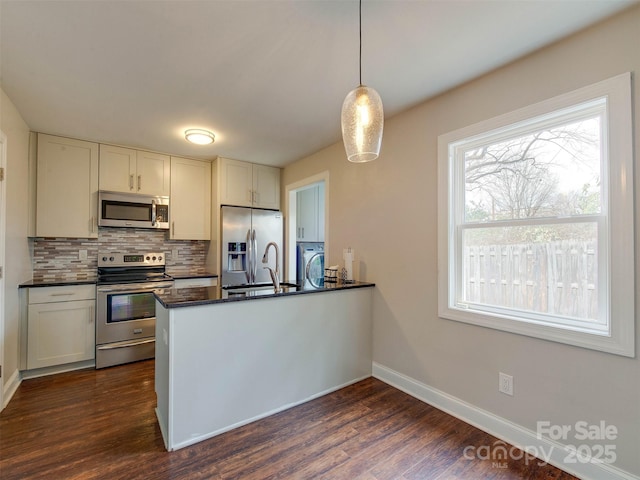 kitchen with a peninsula, dark wood-type flooring, appliances with stainless steel finishes, tasteful backsplash, and dark countertops