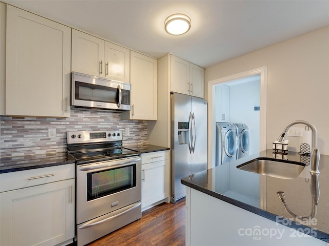 kitchen with stainless steel appliances, a sink, washer and dryer, decorative backsplash, and dark wood-style floors