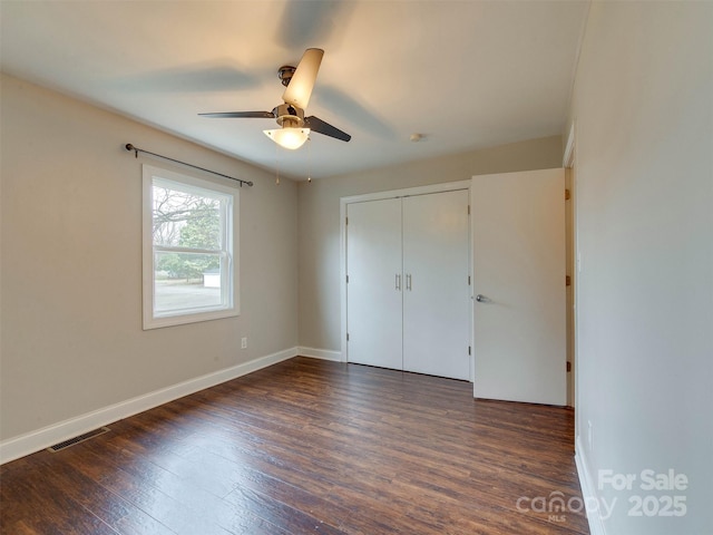 unfurnished bedroom with ceiling fan, dark wood-type flooring, visible vents, baseboards, and a closet