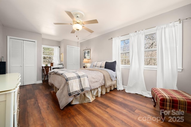 bedroom with baseboards, dark wood finished floors, a ceiling fan, and multiple closets