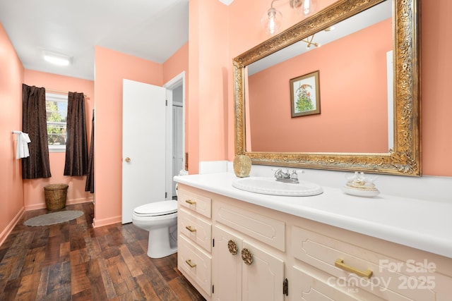 bathroom featuring toilet, baseboards, wood finished floors, and vanity