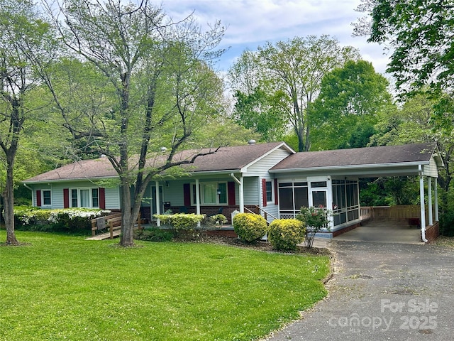 ranch-style house featuring asphalt driveway, a front yard, a carport, covered porch, and a shingled roof
