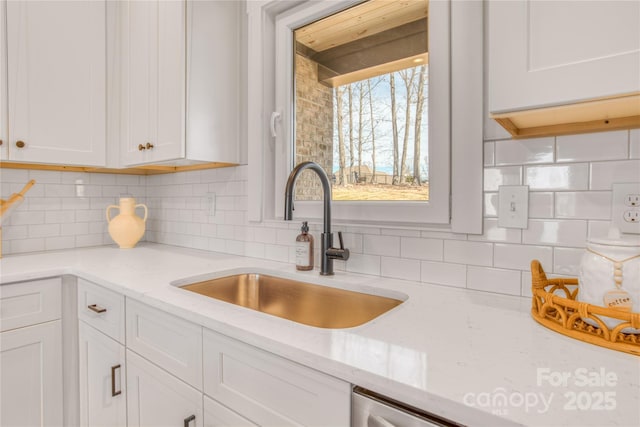 kitchen with light stone counters, white cabinetry, a sink, and decorative backsplash