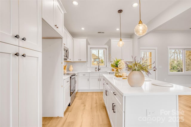 kitchen with light wood finished floors, tasteful backsplash, appliances with stainless steel finishes, a center island, and light countertops