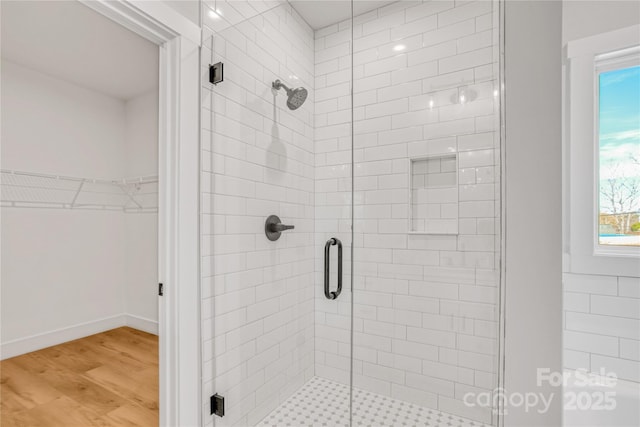 full bath featuring wood finished floors, a stall shower, and a walk in closet