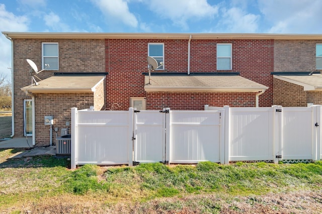 exterior space with cooling unit, brick siding, fence, a lawn, and a gate