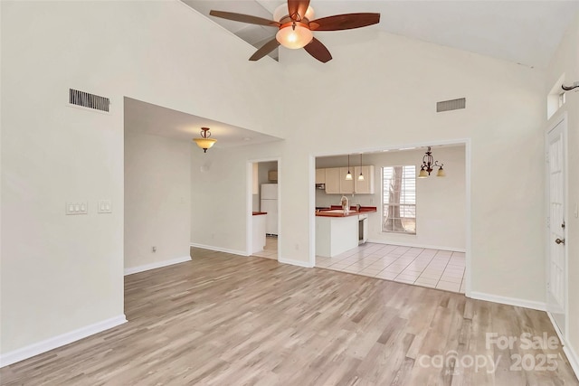 unfurnished living room with light wood-type flooring, high vaulted ceiling, baseboards, and visible vents