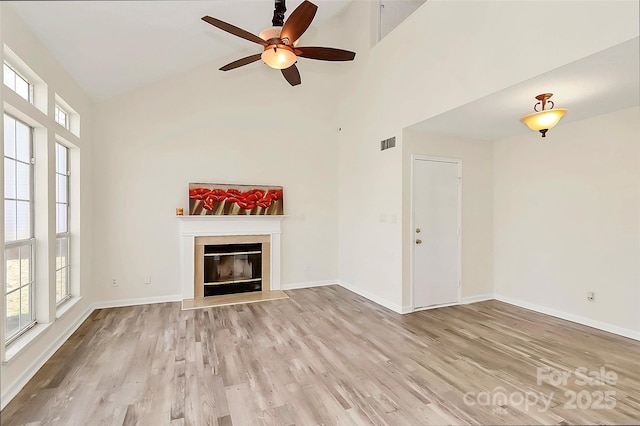 unfurnished living room with a towering ceiling, a glass covered fireplace, light wood-style flooring, and baseboards