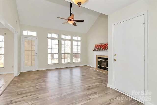 unfurnished living room with light wood finished floors, a fireplace with flush hearth, a ceiling fan, and a wealth of natural light