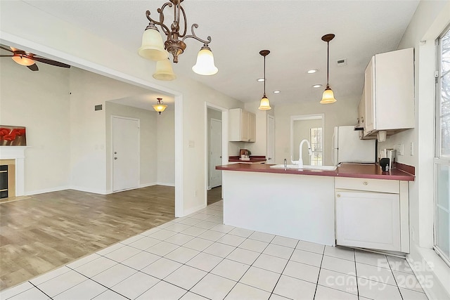 kitchen with a fireplace with flush hearth, a sink, freestanding refrigerator, dark countertops, and decorative light fixtures