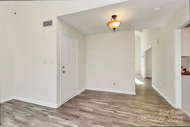 unfurnished room featuring wood finished floors, visible vents, and baseboards