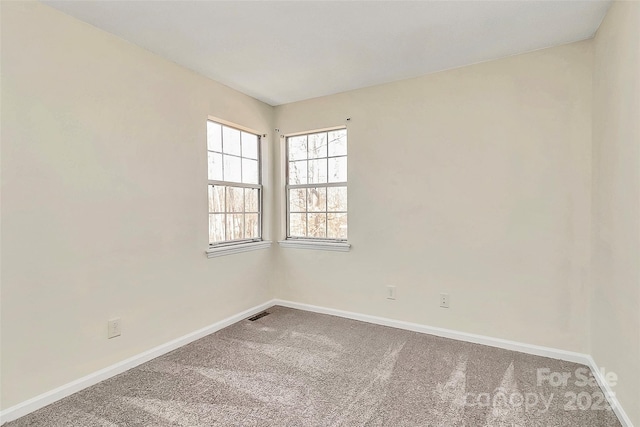 empty room with carpet, visible vents, and baseboards