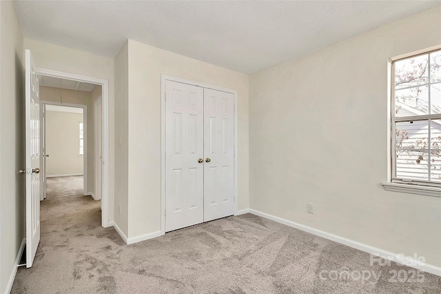 unfurnished bedroom featuring attic access, light carpet, a textured ceiling, and baseboards