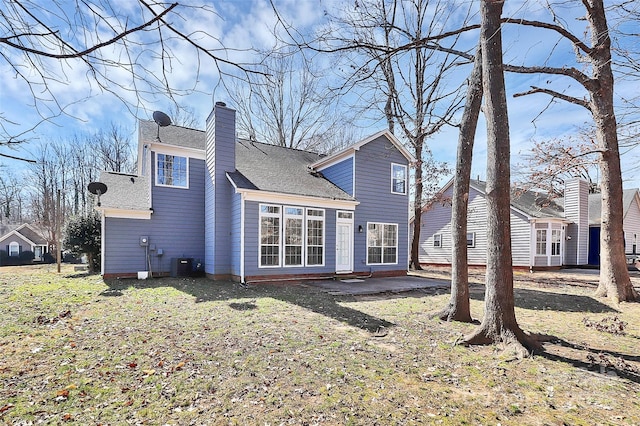 rear view of house featuring a shingled roof, a chimney, central AC, and a yard