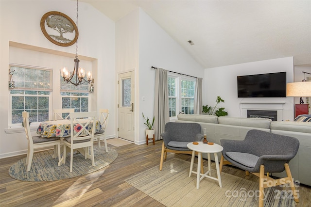 living room with baseboards, a glass covered fireplace, wood finished floors, an inviting chandelier, and high vaulted ceiling