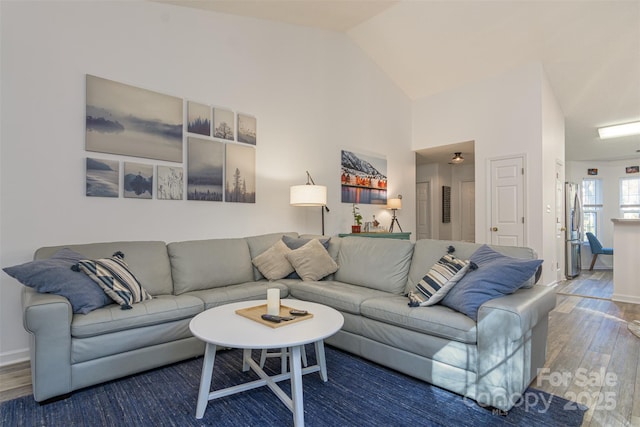 living area with high vaulted ceiling, wood finished floors, and baseboards