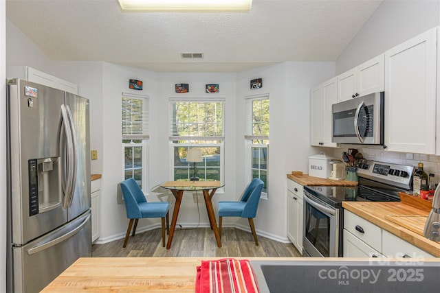 kitchen featuring light wood-style flooring, butcher block counters, visible vents, white cabinets, and appliances with stainless steel finishes