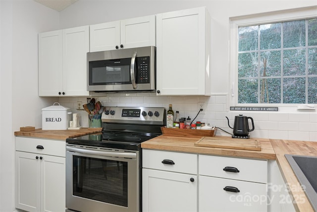 kitchen featuring butcher block counters, appliances with stainless steel finishes, white cabinets, and backsplash