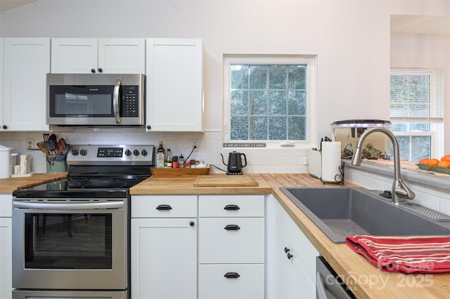 kitchen with a sink, appliances with stainless steel finishes, backsplash, and butcher block counters