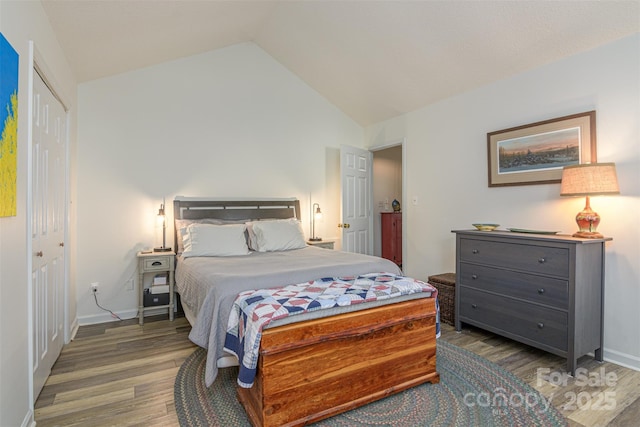 bedroom featuring a closet, vaulted ceiling, baseboards, and wood finished floors