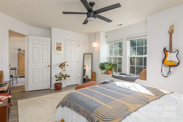 bedroom featuring a ceiling fan, a textured ceiling, visible vents, and wood finished floors