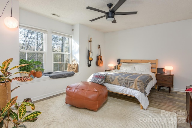 bedroom featuring a textured ceiling, wood finished floors, a ceiling fan, visible vents, and baseboards