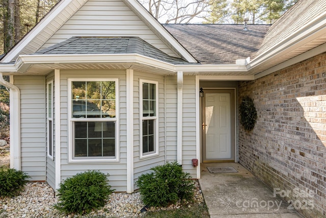 doorway to property featuring brick siding and roof with shingles