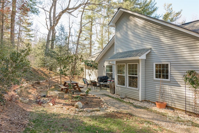 view of property exterior featuring a shingled roof and a patio