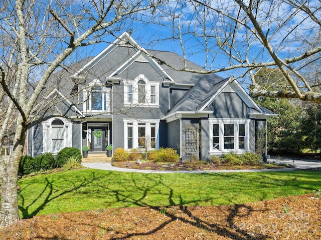 traditional-style home with roof with shingles, a front lawn, and stucco siding