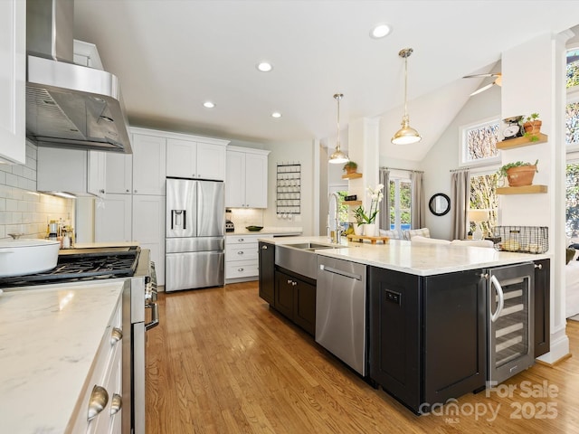 kitchen with light wood-style floors, wall chimney exhaust hood, white cabinetry, stainless steel appliances, and wine cooler