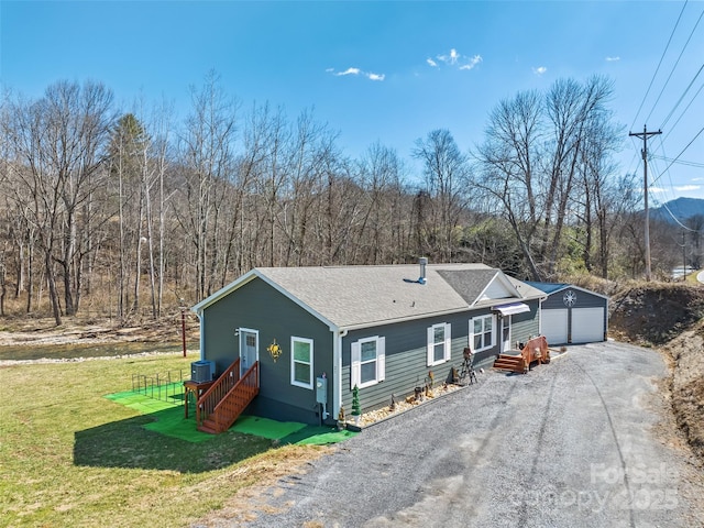 view of front of home featuring an outbuilding, central air condition unit, a shingled roof, a front yard, and driveway