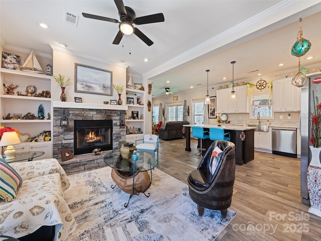 living area with a fireplace, visible vents, light wood-style flooring, ornamental molding, and ceiling fan