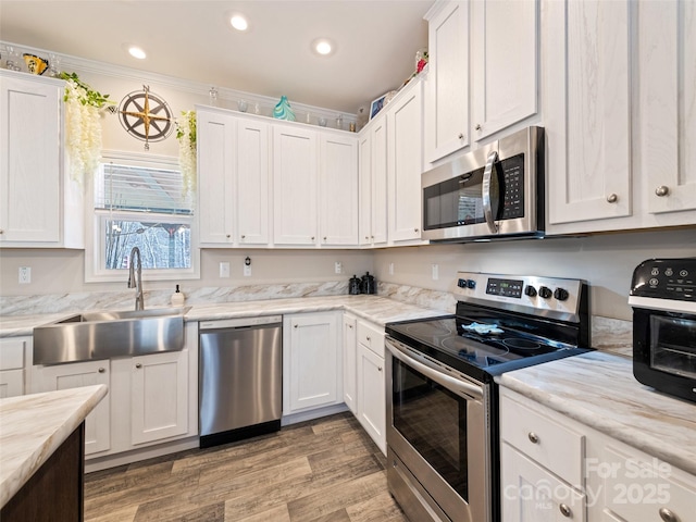 kitchen featuring light wood-style flooring, ornamental molding, stainless steel appliances, white cabinetry, and a sink