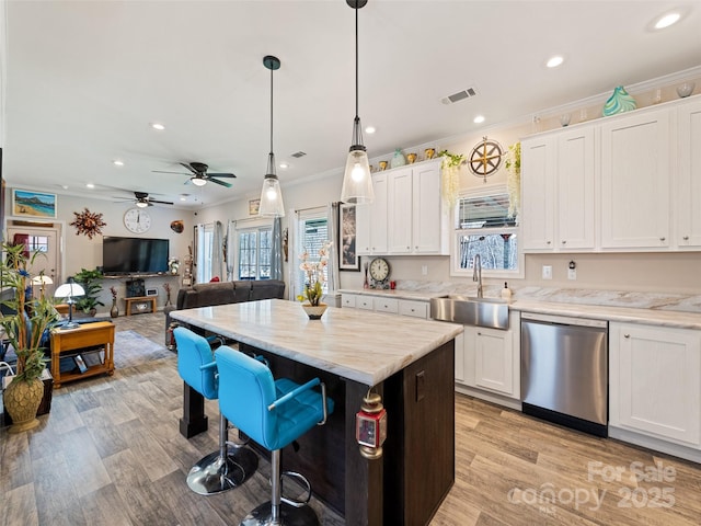 kitchen featuring stainless steel dishwasher, a breakfast bar area, a sink, and white cabinetry